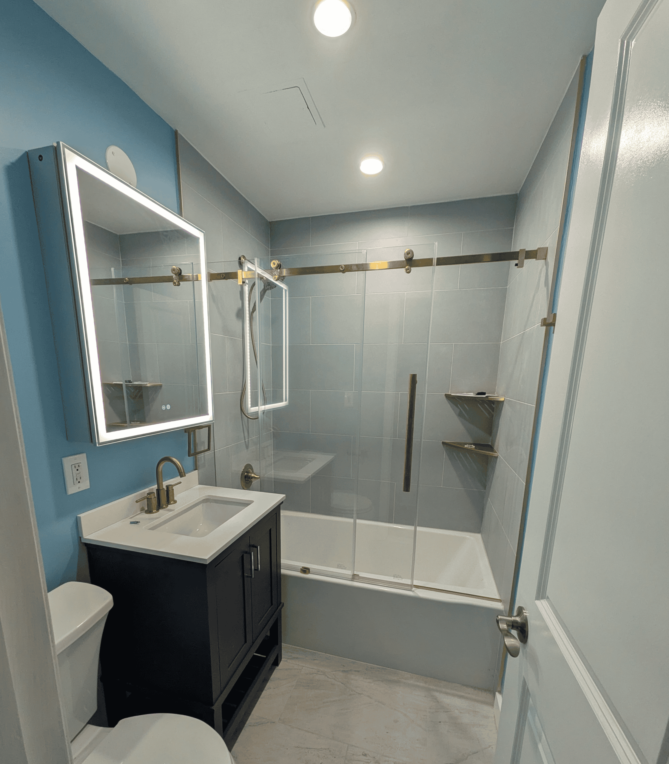 Example Co bathroom with blue walls, glass shower doors, and brass fixtures.